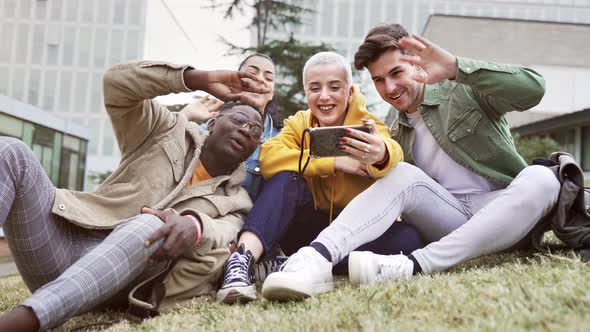 Happy Young Student Friends Sitting on Grass Doing Online Video Call with Mobile Phone at