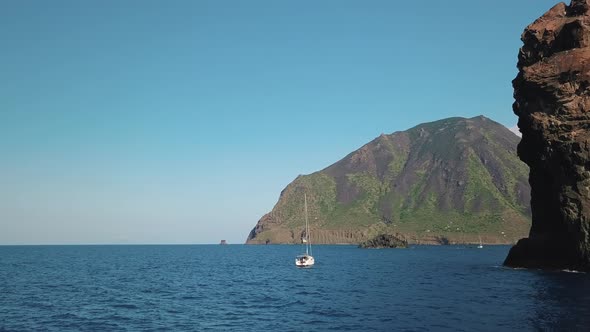 Aerial View on Rocks and Lipari Island, White Sailboat with Flag of Ukraine and People on Board