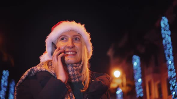 a woman chatting on her smartphone wearing a Santa hat is a night city.