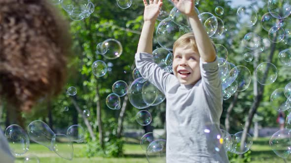 Lovely Kids Running and Catching Bubbles at Warm Sunny Day alt