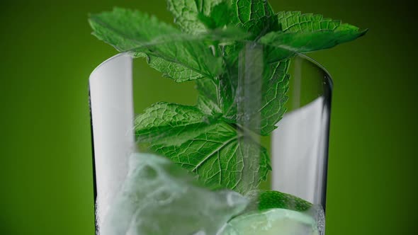 Leaf of Mint Drops to the Highbowl Glass with Cocktail and Ice Cubes on the Green Background 1080p