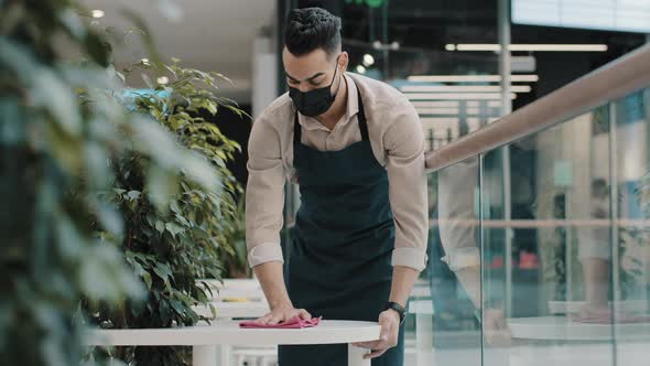 Young Guy Waiter Wipes Table in Cafe Food Service Worker in Medical Mask Does Cleaning Before