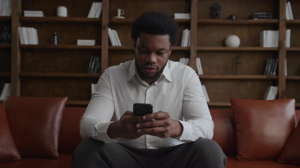 Young Adult Africanamerican Man Browsing on His Smartphone in Loft Apartment