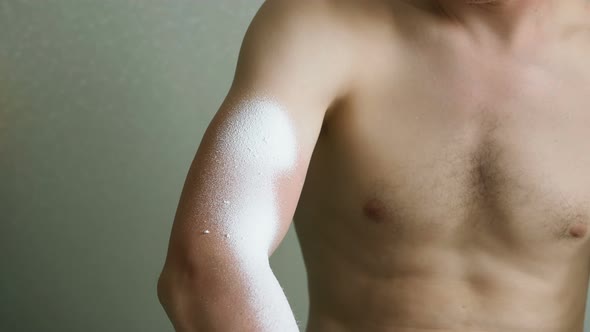 Man Applies Spray To Cure Red Burned Skin Near Grey Wall