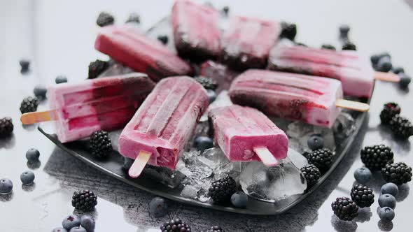 Homemade Fresh Frozen Blueberry and Blackberry Popsicles on Black Plate with Ice Sitting on Stone