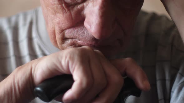 Close-up portrait of caucasian sad pensioner 70 years old sitting meditating with walking stick. Slo