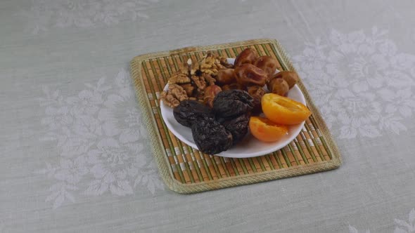 Apricots Prunes Dates Walnuts on a White Saucer Standing on a Bamboo Napkin