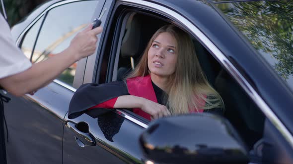 Charming Slim Woman in Graduation Gown Sitting in Car As Unrecognizable Parent Passing Key in Slow