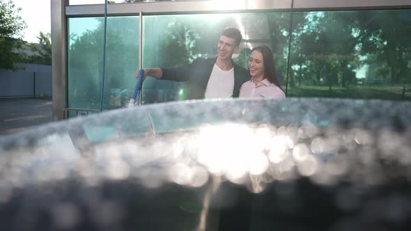 Positive Man Spraying Water on Automobile in Slow Motion As Happy Woman Smiling Admiring Clean