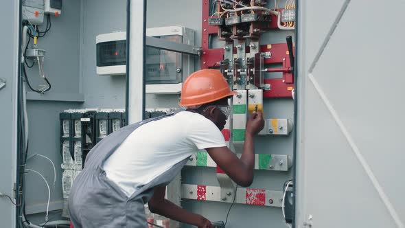 African American Man in Overalls Standing Near Switchgear at Solar Station