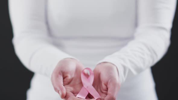 Mid section of woman holding a pink ribbon against black background