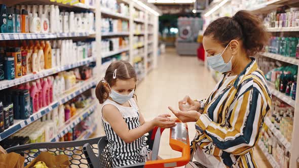 Child is Sitting in Shopping Cart and Makes Disinfection of Hands in Supermarket