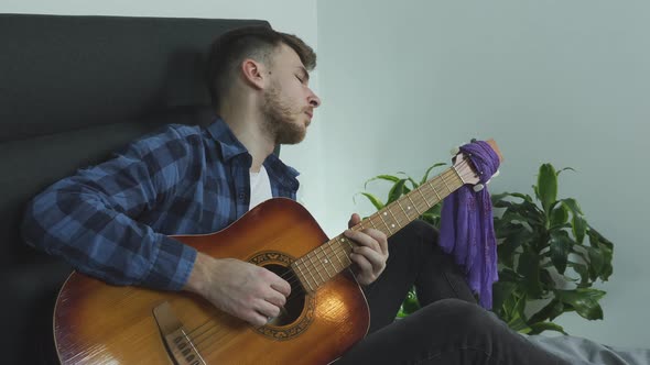 Man plays song on acoustic guitar on bed in modern living room. Music concept