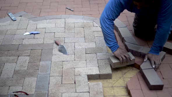 Steadicam shot of stone mason fitting and marking brick pavers for cutting for a two-tone emblem des
