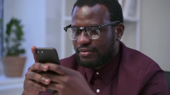 African Man Looks at Smartphone and Clicks on Screen in Office Interior Spbas