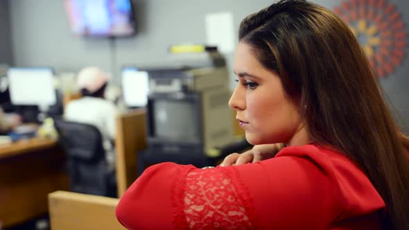 Close up of woman in red shirt leaning against cubical and observes coworkers