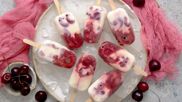 Fresh Cream and Cherry Homemade Popsicles Placed on White Ceramic Plate with Fruits and Textile