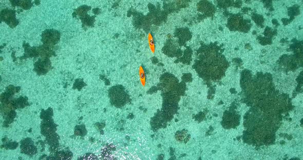 Aerial drone view of a man and woman couple kayaking around a tropical island.