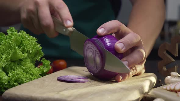 Chef Cuts the Red Onion By the Sharp Knife on the Wooden Board at the Kitchen, Close Up Video of