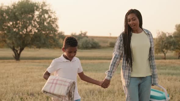 A boy is walking in a field holding hand with his mother