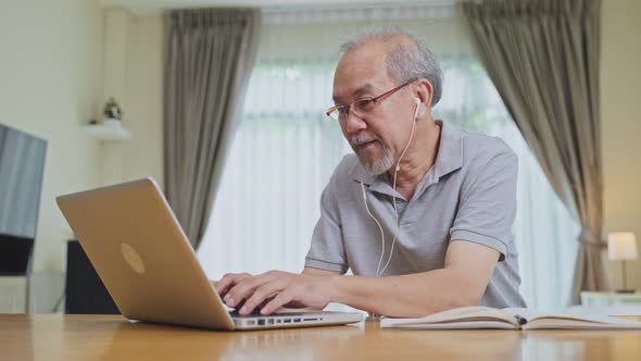 Home office of Asian Senior elderly business man work online with laptop computer in living room.