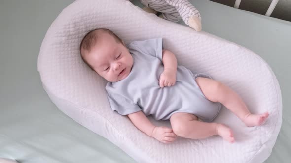 Newborn Baby Boy Lying in Nursery Cocoon with Blue Clothes on Bed in Bedroom at Home Looking to