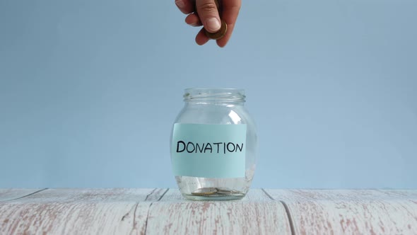 Hand throwing coins in transparent jar with inscription donation