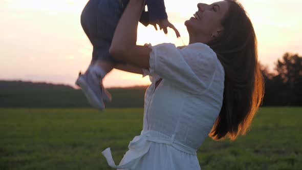 Loving Mother Throws Her Baby Up In The Air Against The Rays At Sunset