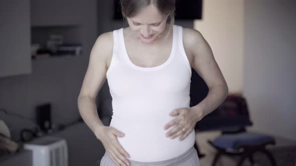 Smiling Pregnant Lady Standing and Rubbing Belly