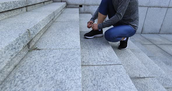 Fitness sports woman tying shoelace and running up stairs in city