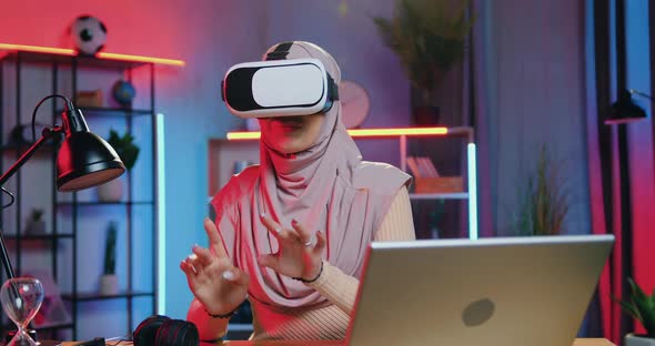 Woman in Hijab at Home in the Evening and Working on Imaginary Screen in Augmented Reality goggles
