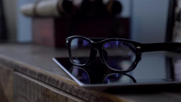 Glasses in Black Rim Lying on a Tablet on a Wooden Dresser in the Room Close Up