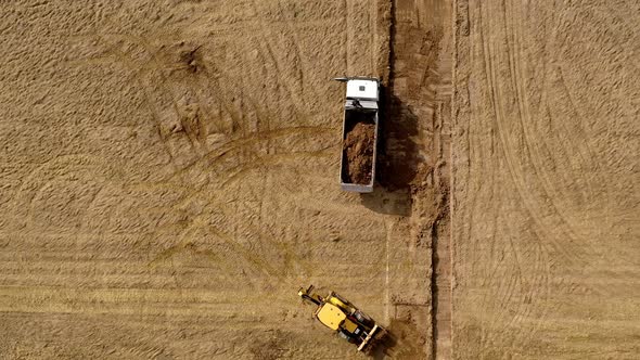 Yellow excavator digs the ground and loads it on a truck. Top view.