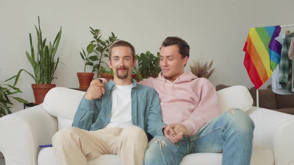 Lgbt Young Handsome Men are Sitting on the Sofa Together Holding Hands and Looking at the Camera