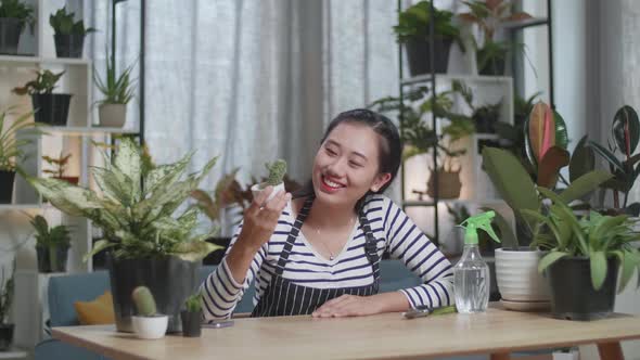 Smiling Asian Woman Looking At Cactus Plant In Hand And Shaking Her Head