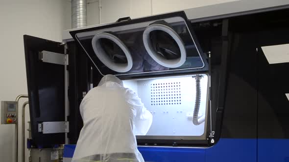 Worker in White Protective Suit Cleans Inside Industrial 3D Printer for Metal