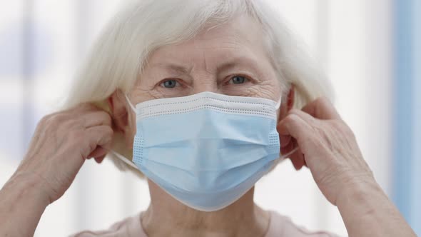 Close Up View of Mature Pensioner Woman with White Hair Taking Off Medical Protective Mask 