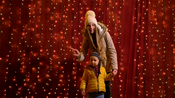 Two teenager posing and waving in front of lights wall at Christmas market.