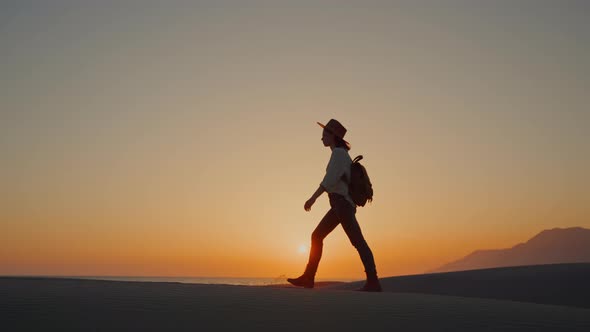 Young woman with camera walking on the sand on the beach at sunset