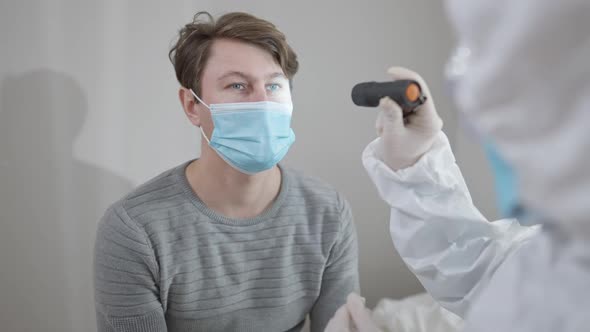 Portrait of Brunette Caucasian Man in Covid19 Face Mask Sitting in Hospital As Unrecognizable Doctor