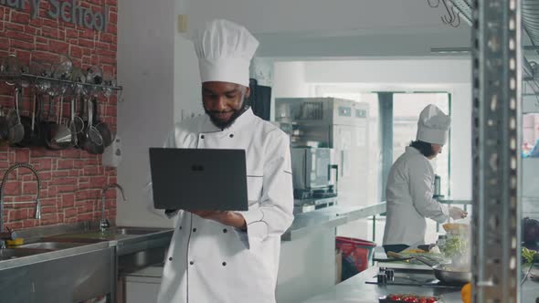 African American Cooker Looking at Laptop Screen to Cook Gourmet Dish