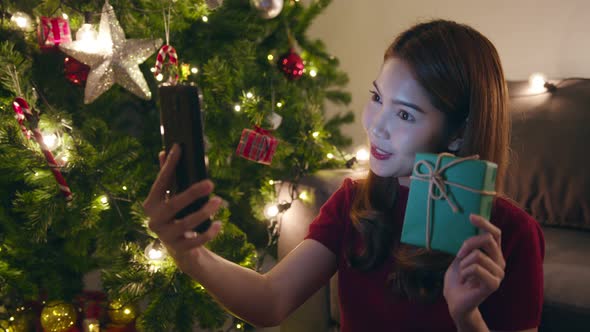 Young Asia female using smart phone video call talking with couple with X'Mas present box.