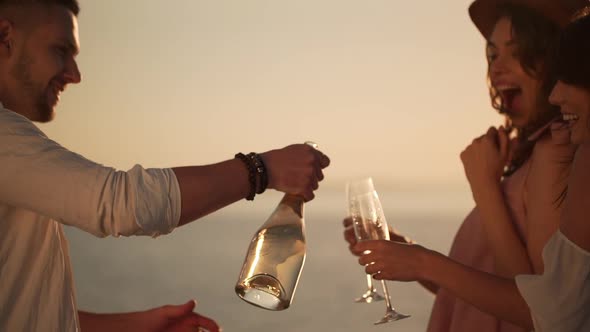 Slow Motion Joyful Guy Opening Bottle of Champagne for Elegant Beautiful Girls Having Fun Together