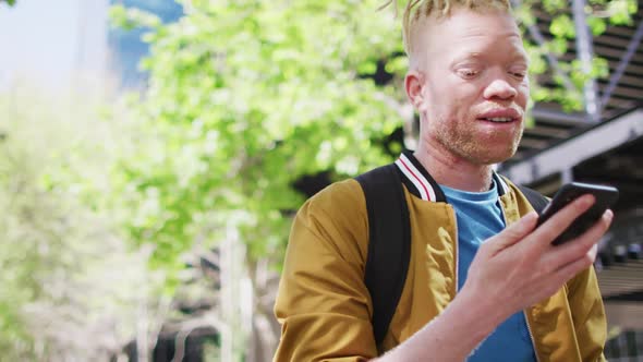 Happy albino african american man with dreadlocks in park talking on smartphone