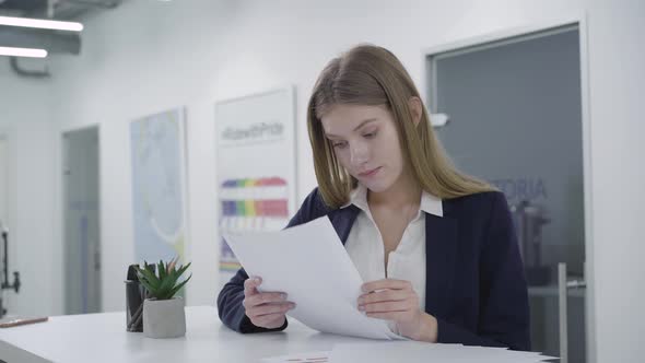 Thoughtful Young Lady in Formal Clothes Attentively Checking Documents in the Office