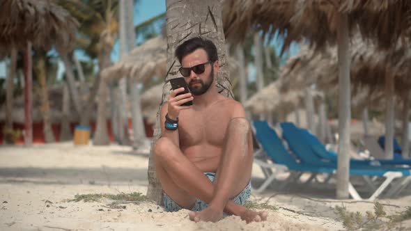 Man Sitting On Palm And Talking On Smartphone On Vacation Lounge Sea. Man Resting On Ocean.