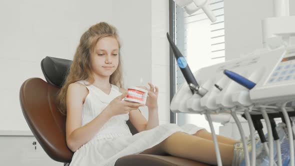 Beautiful Little Girl Smiling Holding Jaw Model Sitting in Dental Chair at the Clinic