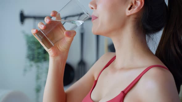 Close up of Asian attractive sport woman drink water after exercise for health care in kitchen.