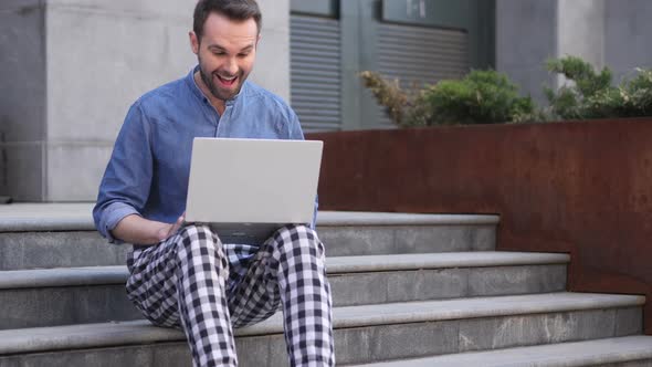 Excited Man Celebrating Success on Laptop Sitting on Stairs