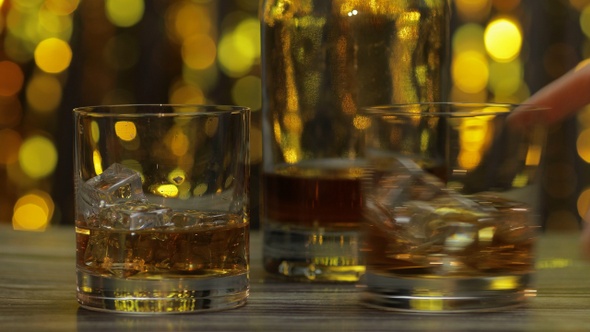 Barman Pushes, Puts Glass with Golden Whiskey, Cognac or Brandy with Ice Cubes on Wooden Table